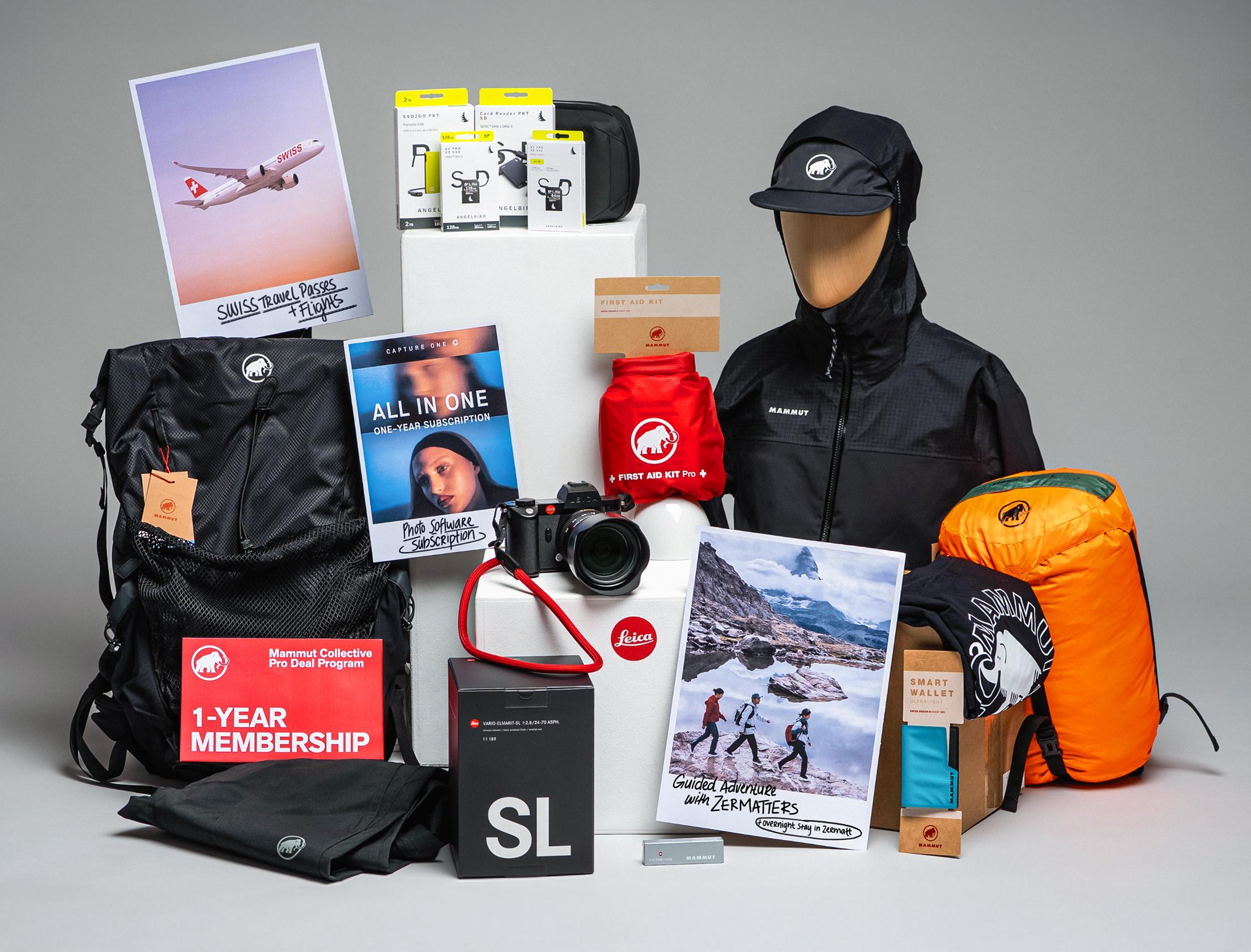 A collection of Mammut outdoor gear, camera equipment, adventure books, and travel essentials arranged on a gray background.