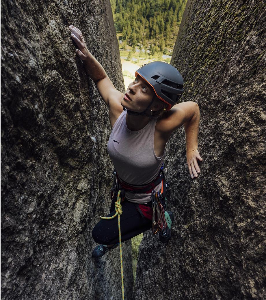 A female climber in Mammut climbing gear ascends a narrow rock crevice, gazing upward with determination during a mountaineering adventure.