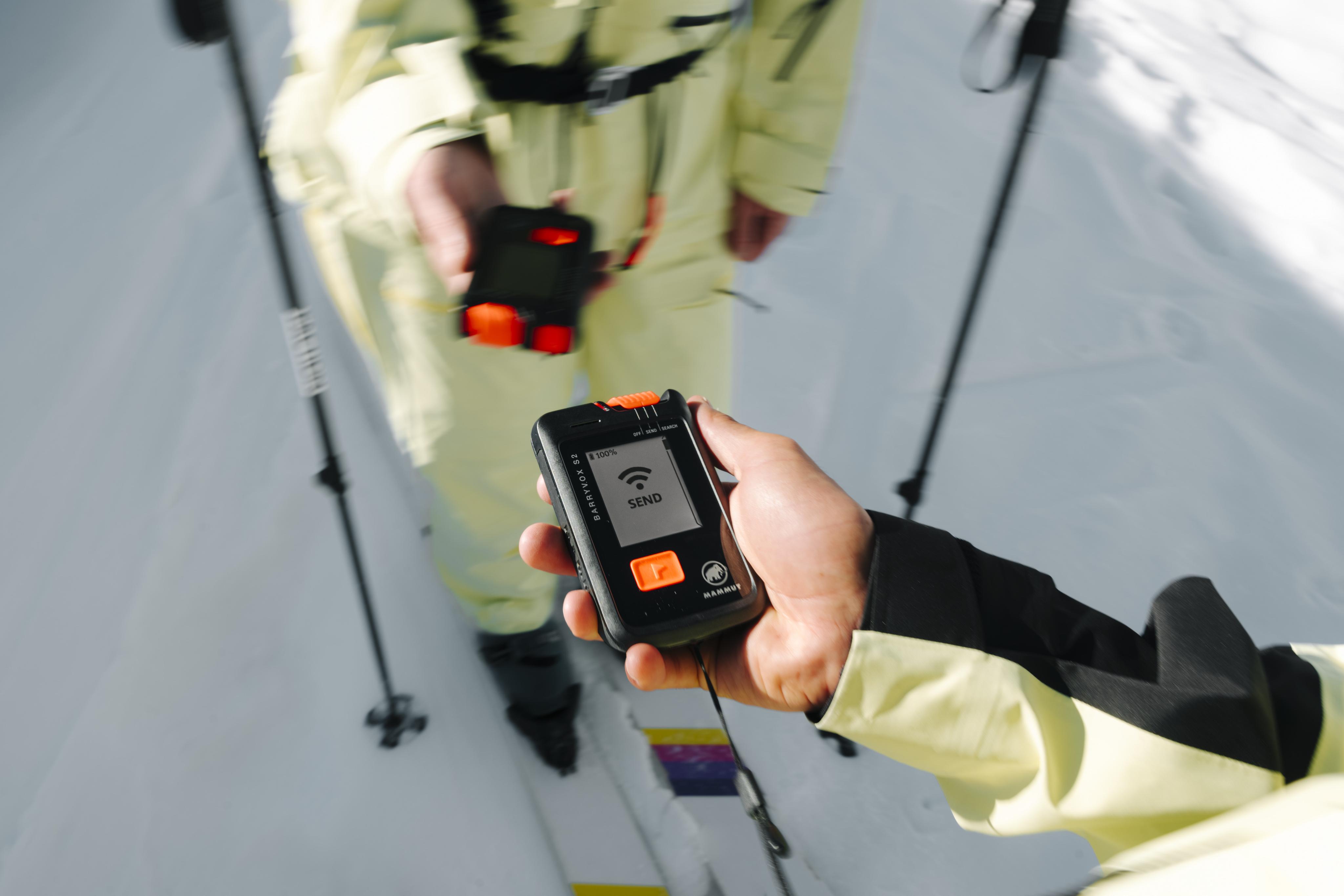 A gloved hand grips a Mammut avalanche transceiver, displaying a distance of 1.2 meters in snowy conditions.