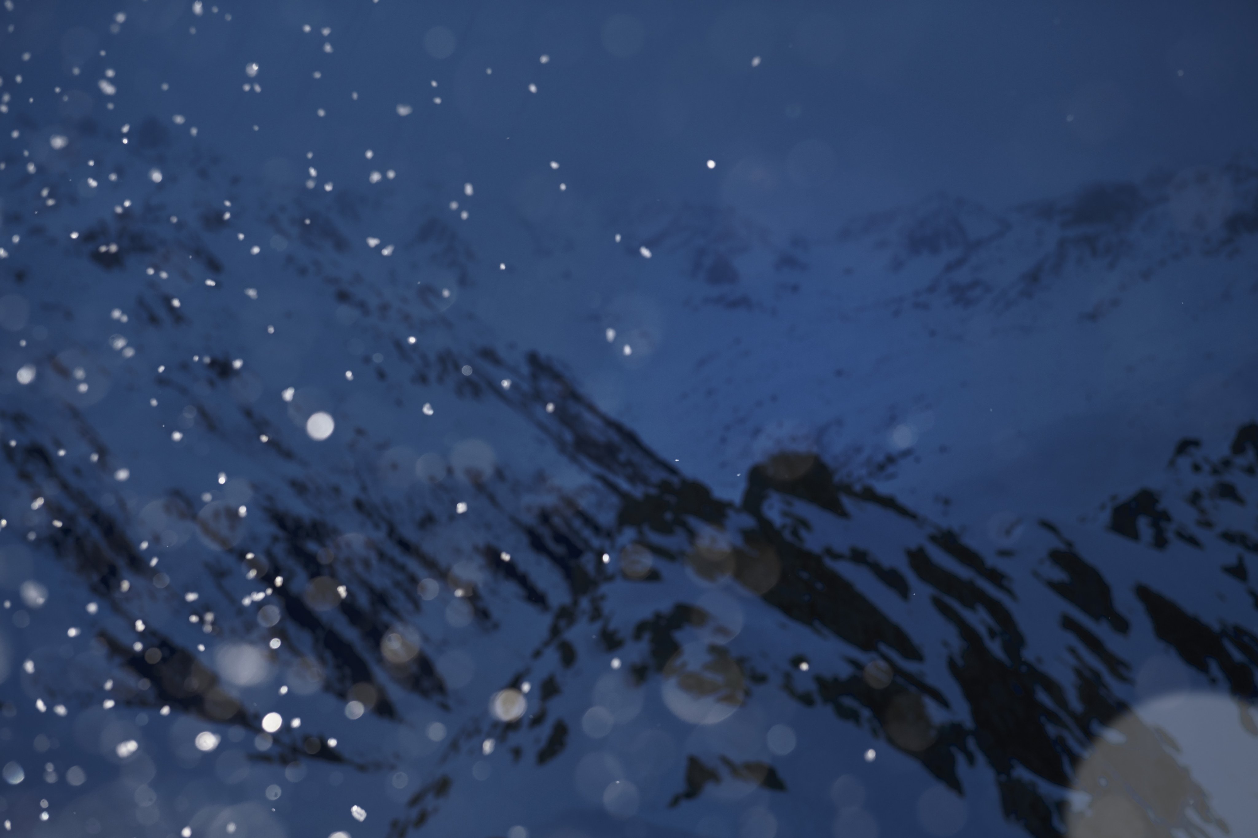 Snow falling in front of snow-covered mountains under a dark, overcast sky at dusk, embodying the adventurous spirit of Mammut mountaineering.