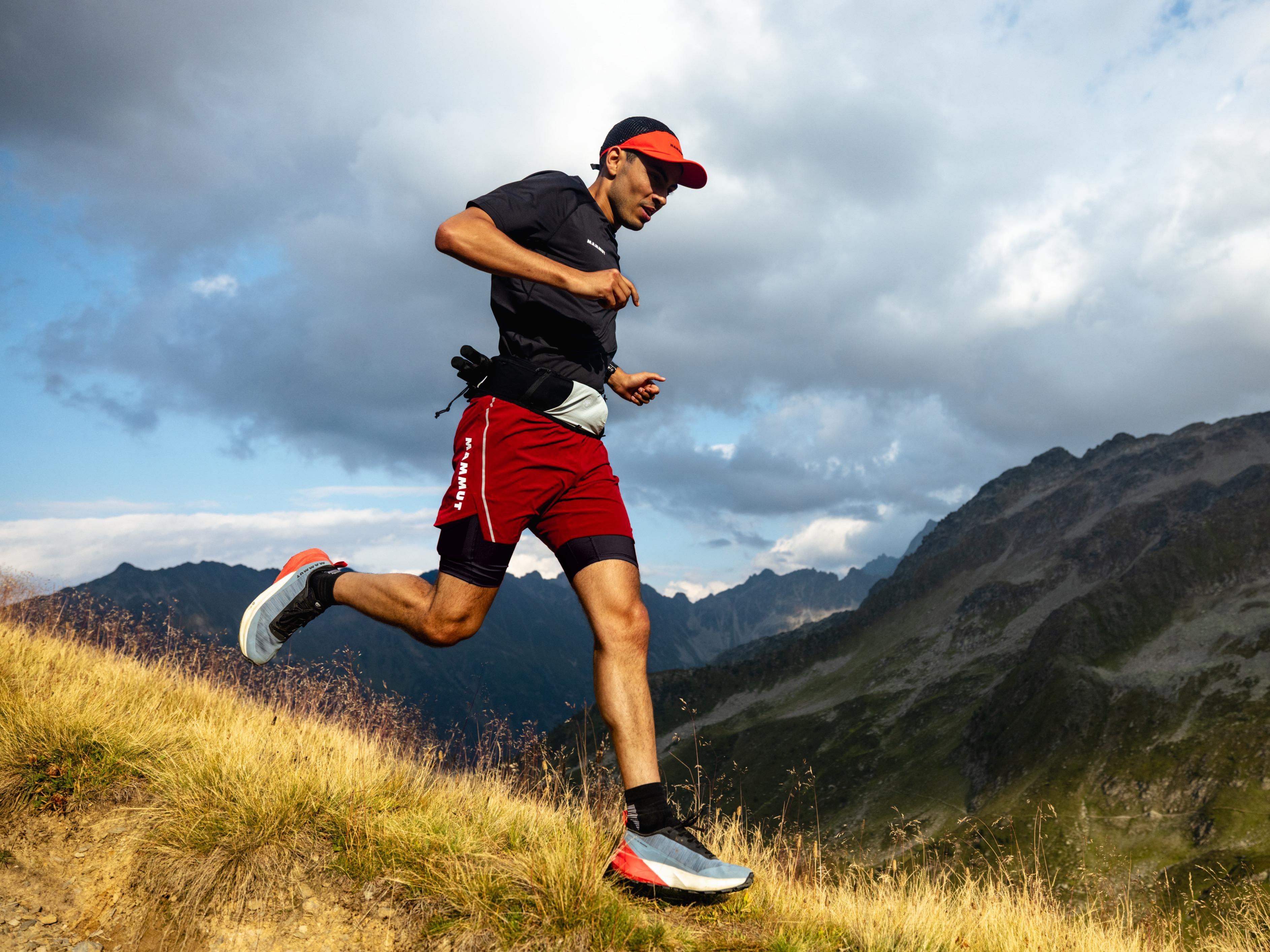 A man resting on a rock in the mountains, wearing outdoor gear and a backpack, possibly from Mammut mountaineering equipment.