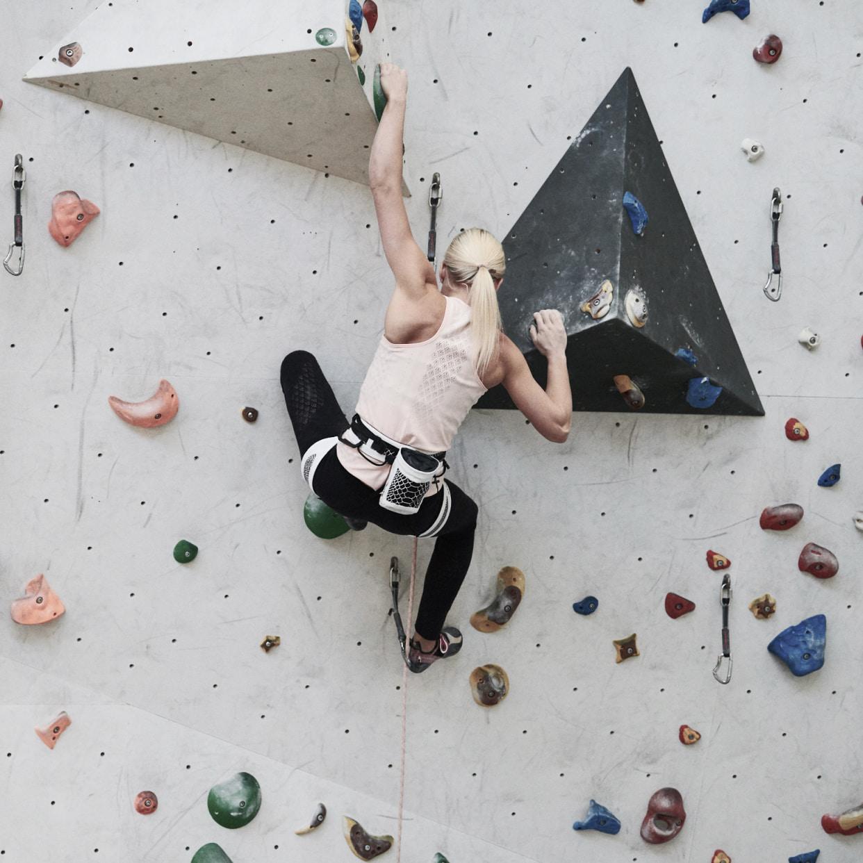 Lucia Capovilla scaling an indoor bouldering wall featuring a variety of colorful holds, wearing Mammut climbing gear.