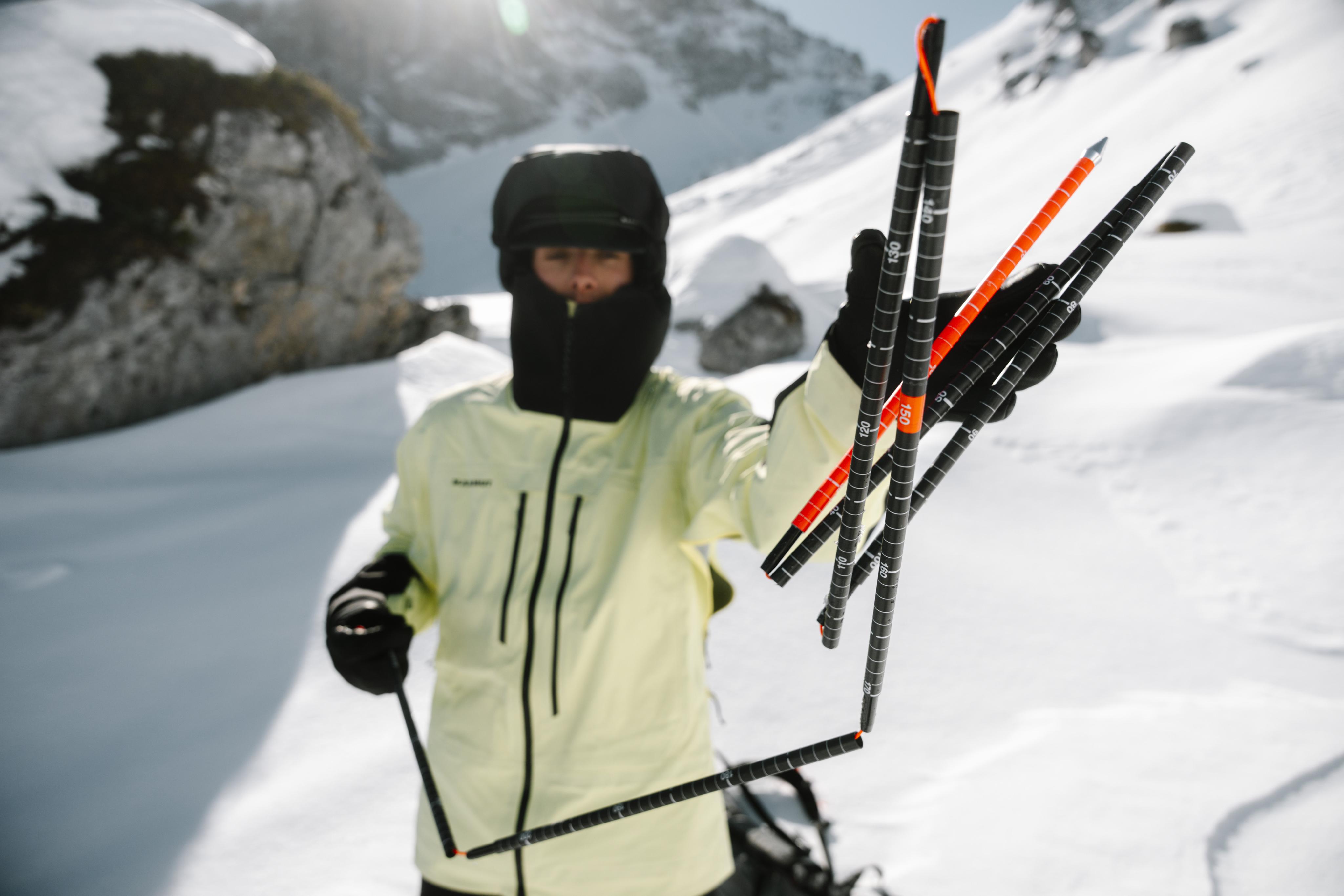 Person wearing a Mammut winter jacket holding ski poles against a cloudy sky.