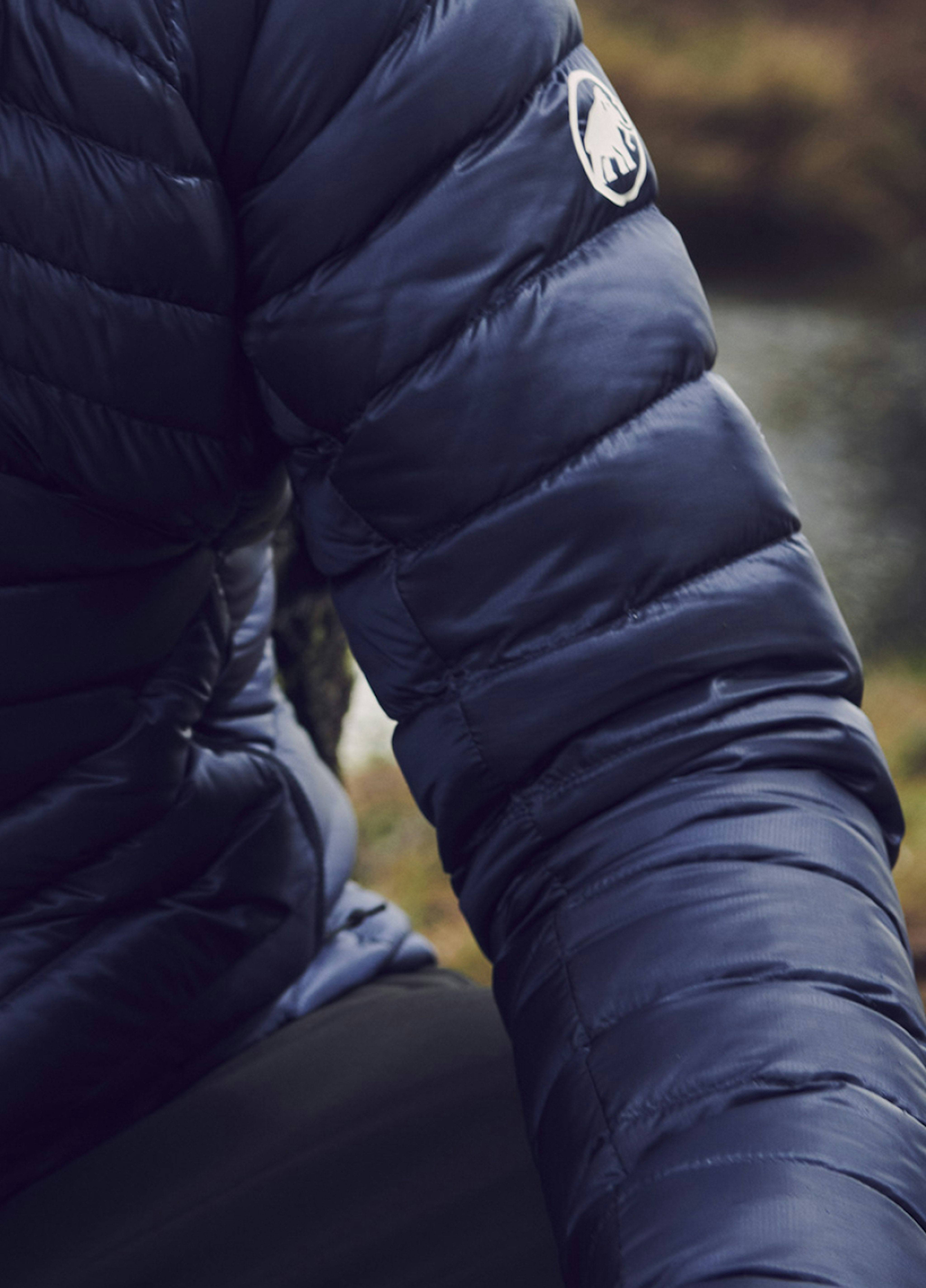 Close-up of a person wearing a Mammut dark blue dry down jacket featuring the iconic embroidered Mammut logo on the sleeve.