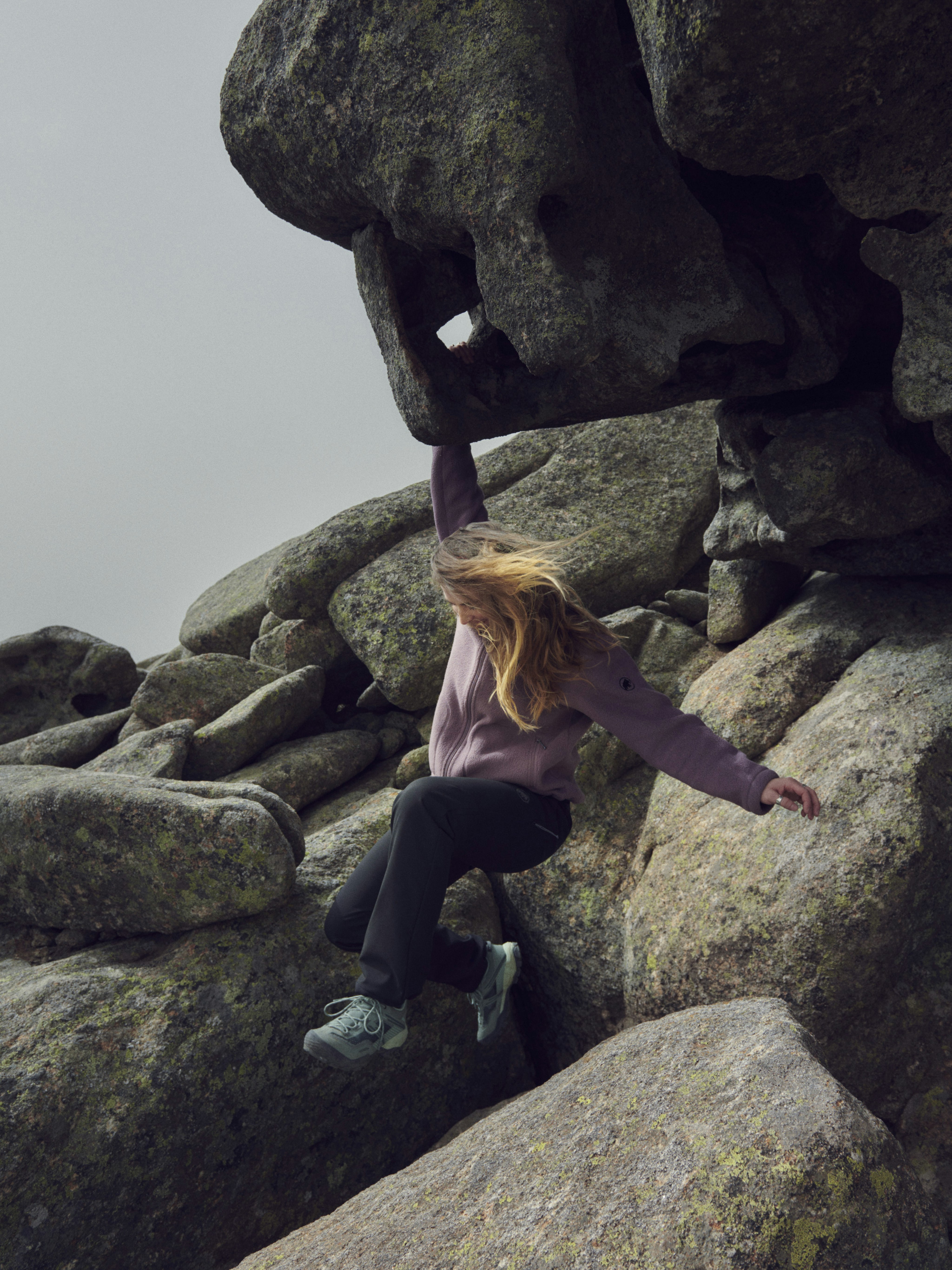 Person wearing Mammut gear hanging onto a rock formation while climbing, surrounded by large boulders.