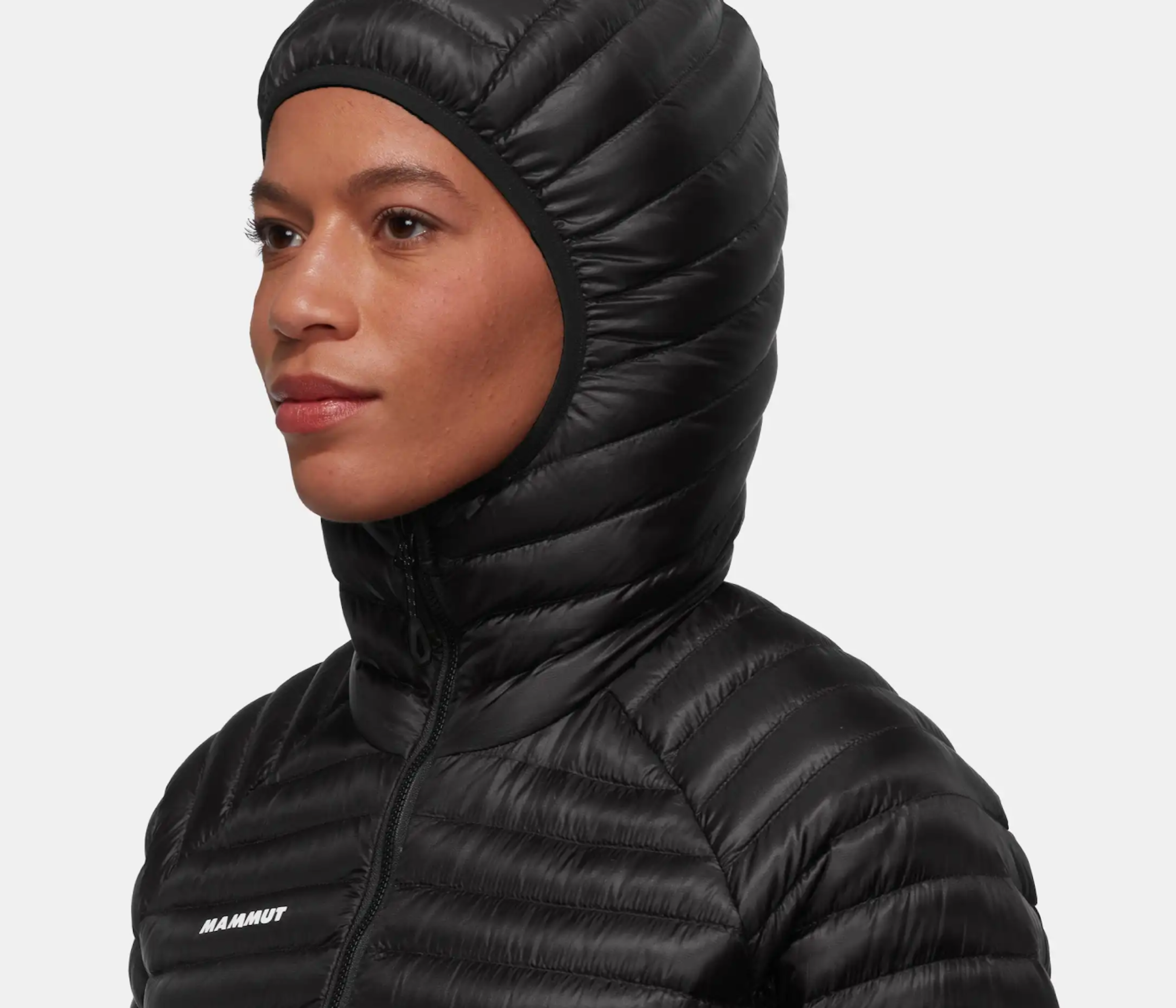 Individual in a Mammut black hooded dry down jacket gazing sideways against a neutral background.