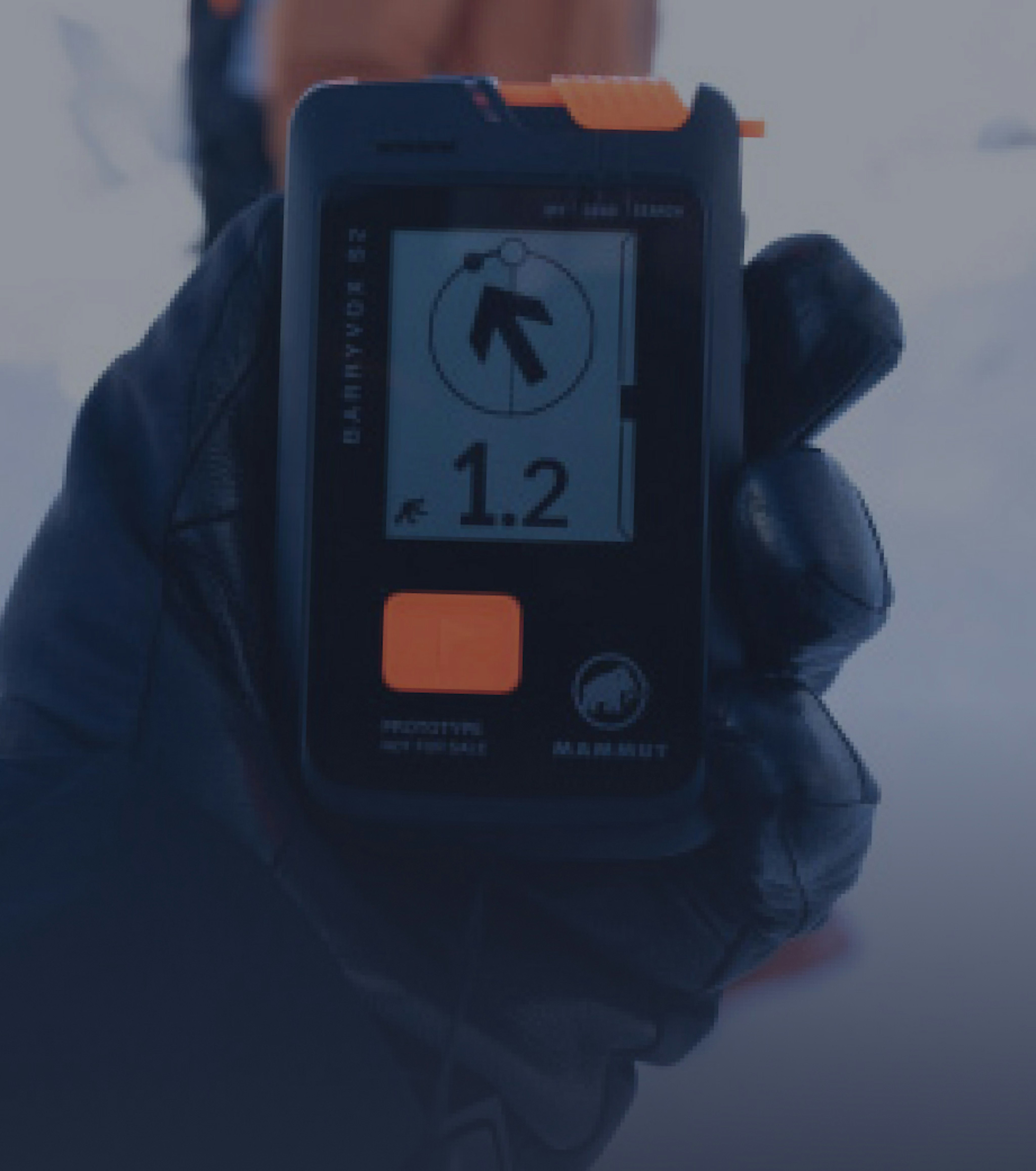 A gloved hand grips a Mammut avalanche transceiver, displaying a distance of 1.2 meters in snowy conditions.