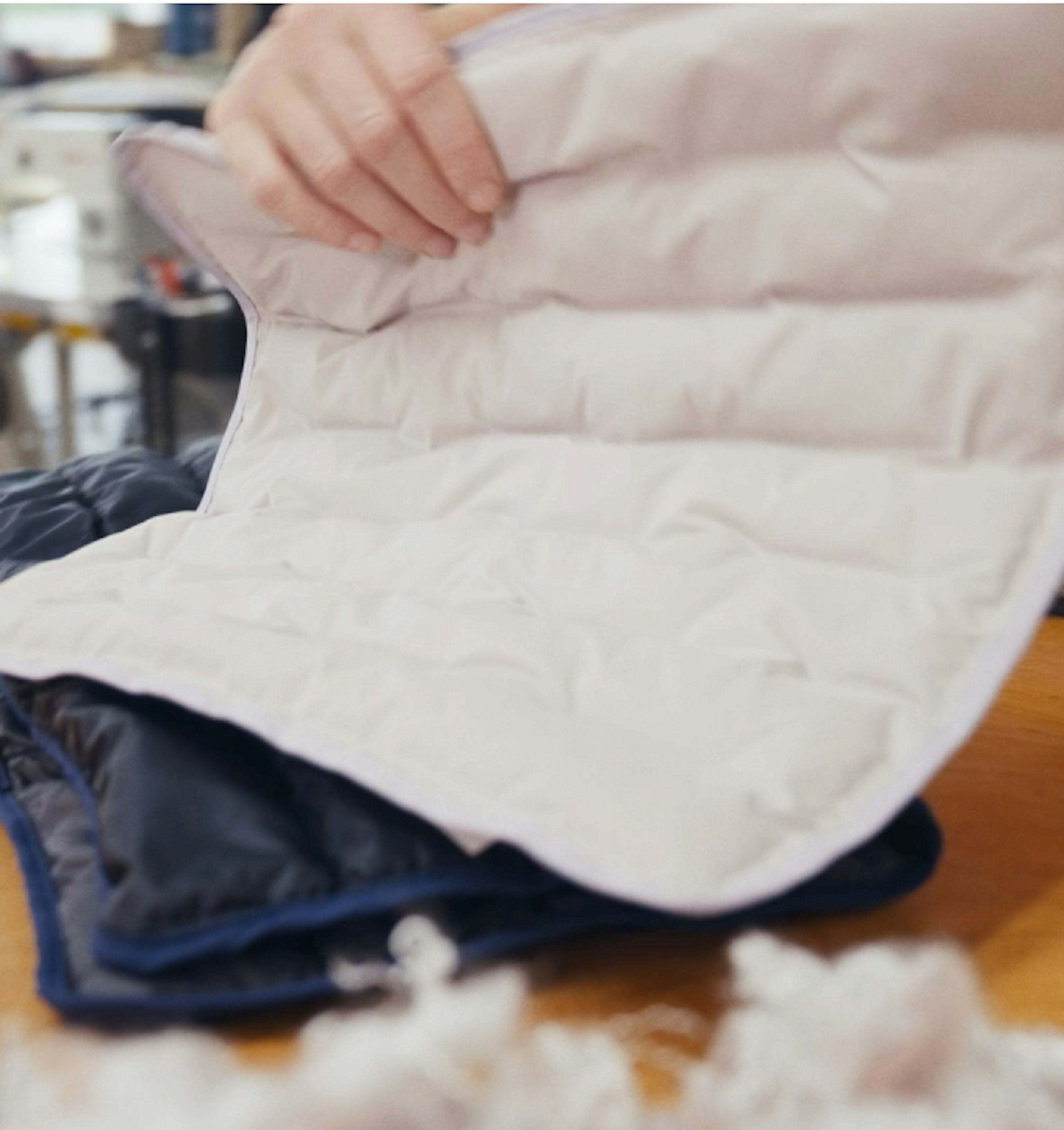 A person examining the inside padding of a quilted Mammut jacket on a table, with fluffy down stuffing visible.