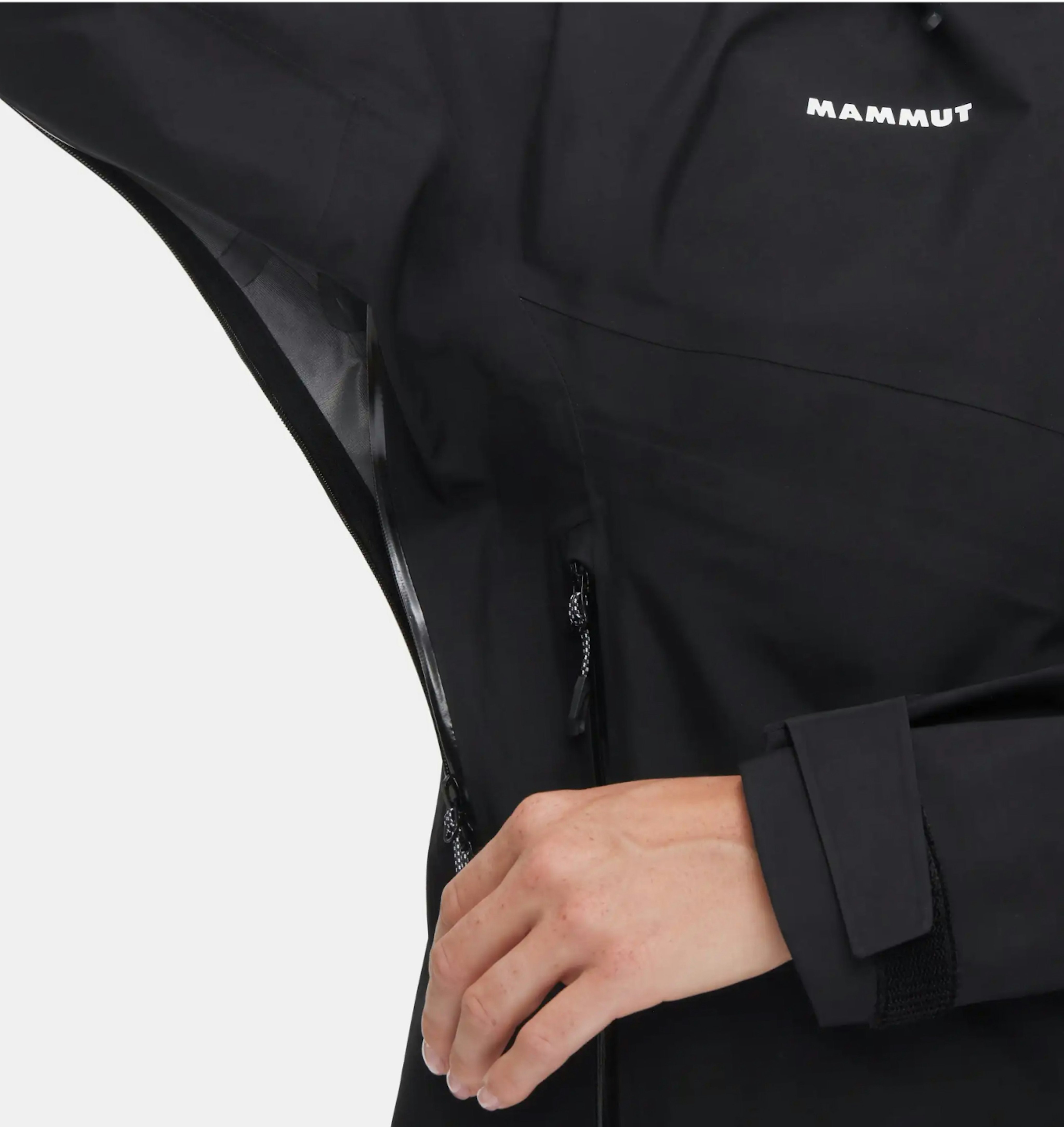 Person unzipping the side vent of a black Mammut mountaineering jacket, showcasing the breathable lining inside.