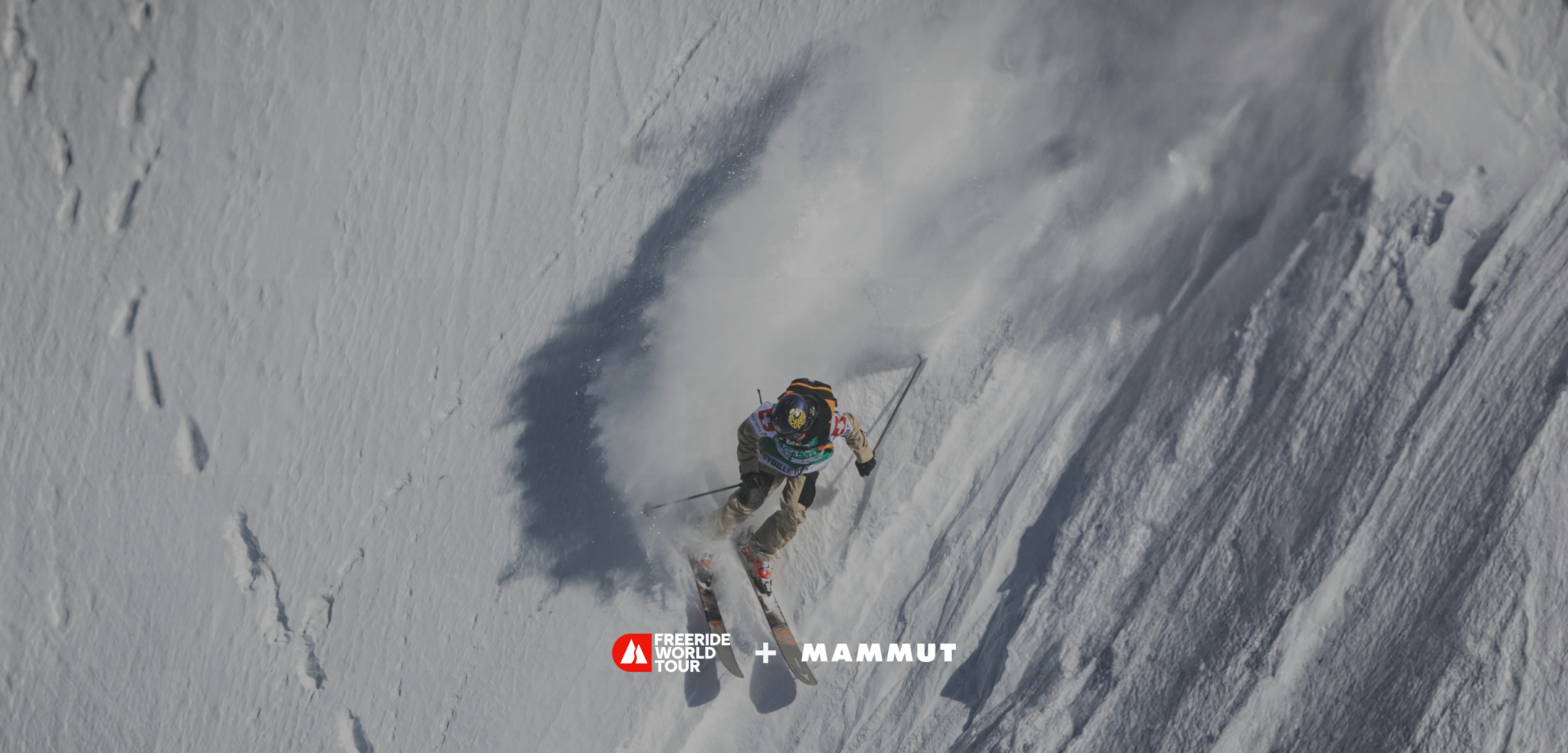 Skier making a sharp turn on a steep snowy slope, leaving a trail of snow, showcasing Mammut gear during the Freeride World Tour.