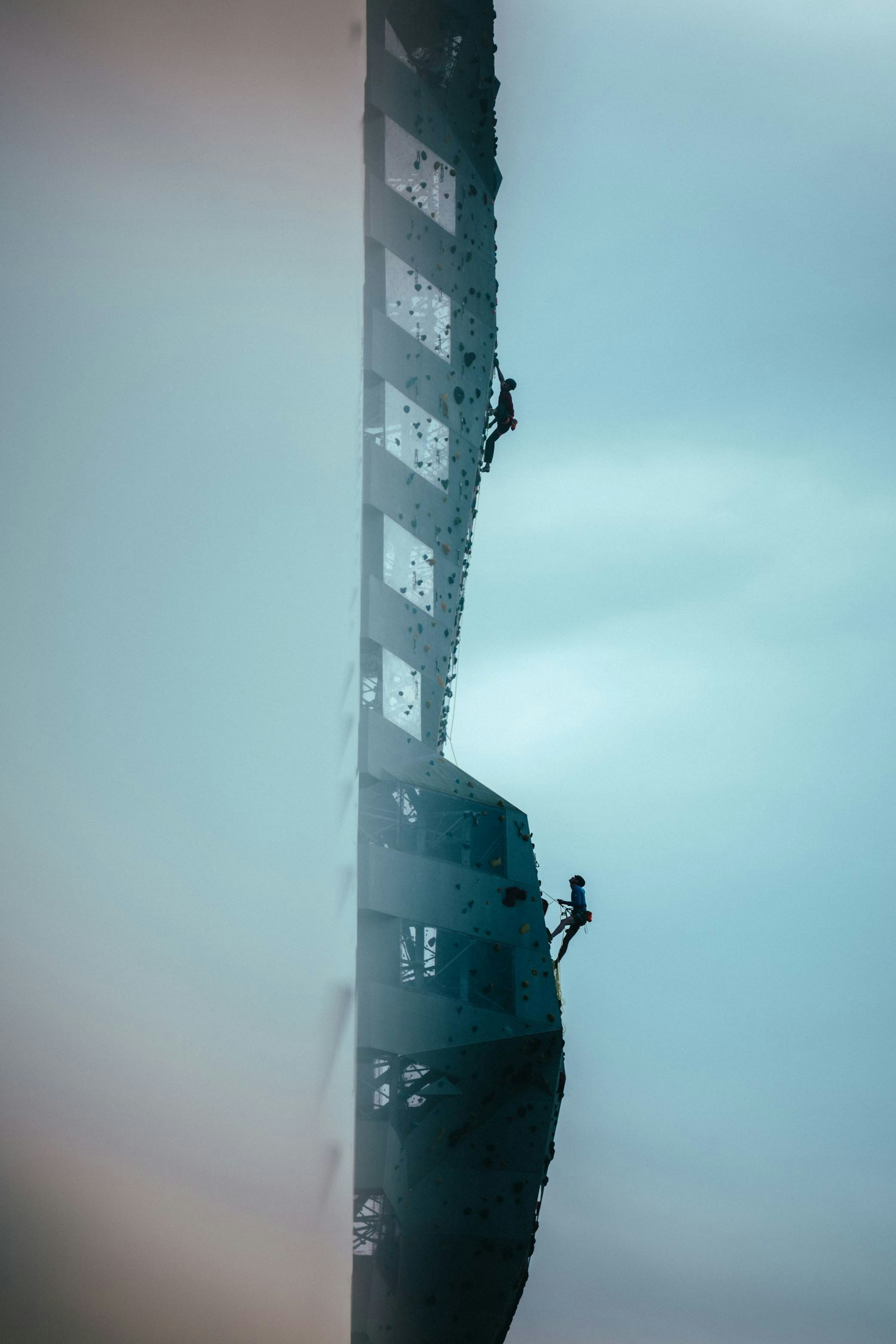 Two climbers scale a towering rock face wearing Mammut gear against a backdrop of a cloudy sky at Copenhill in Denmark.