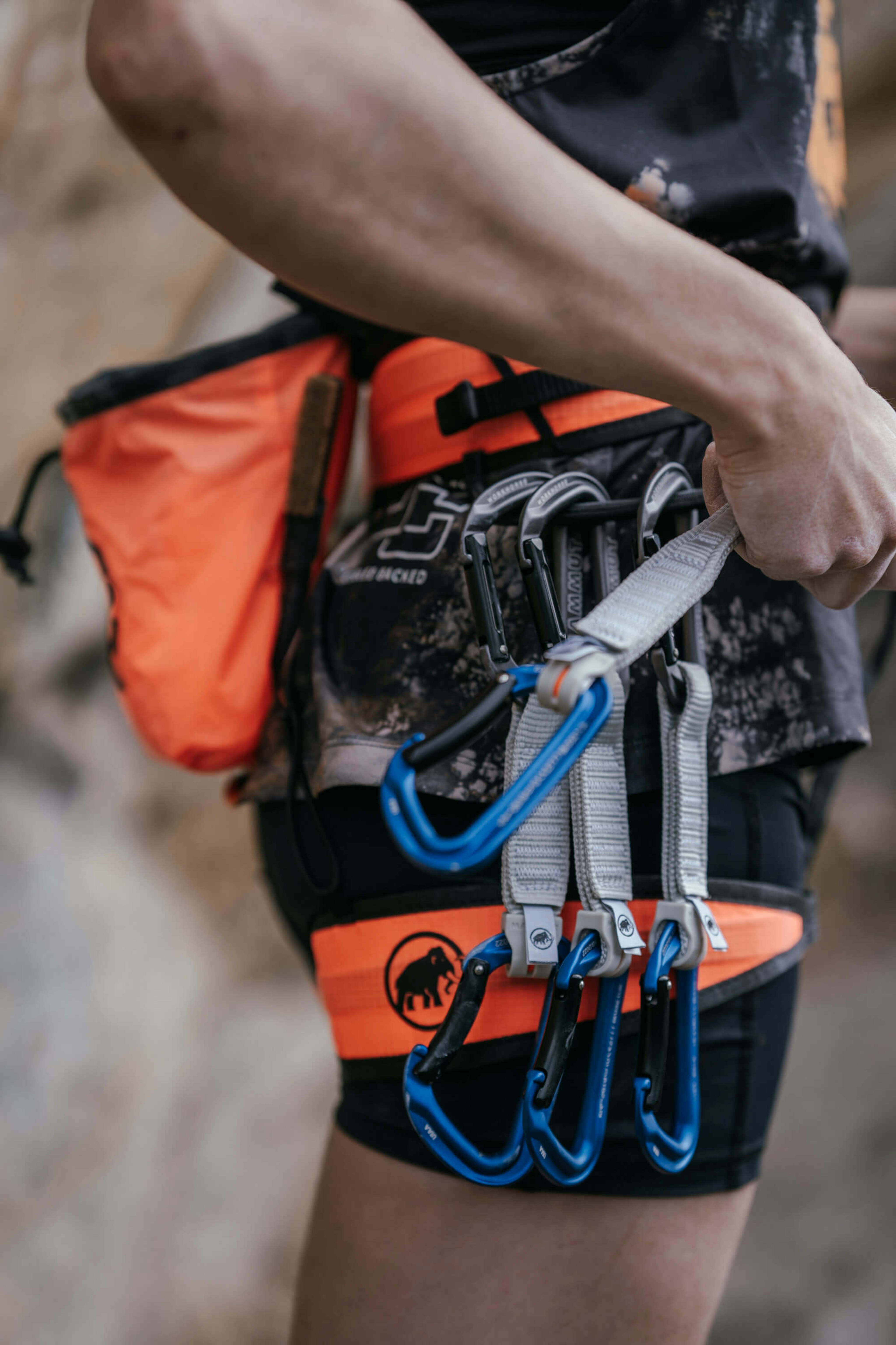 Person outfitted in Mammut climbing gear, including an orange harness with attached carabiners.