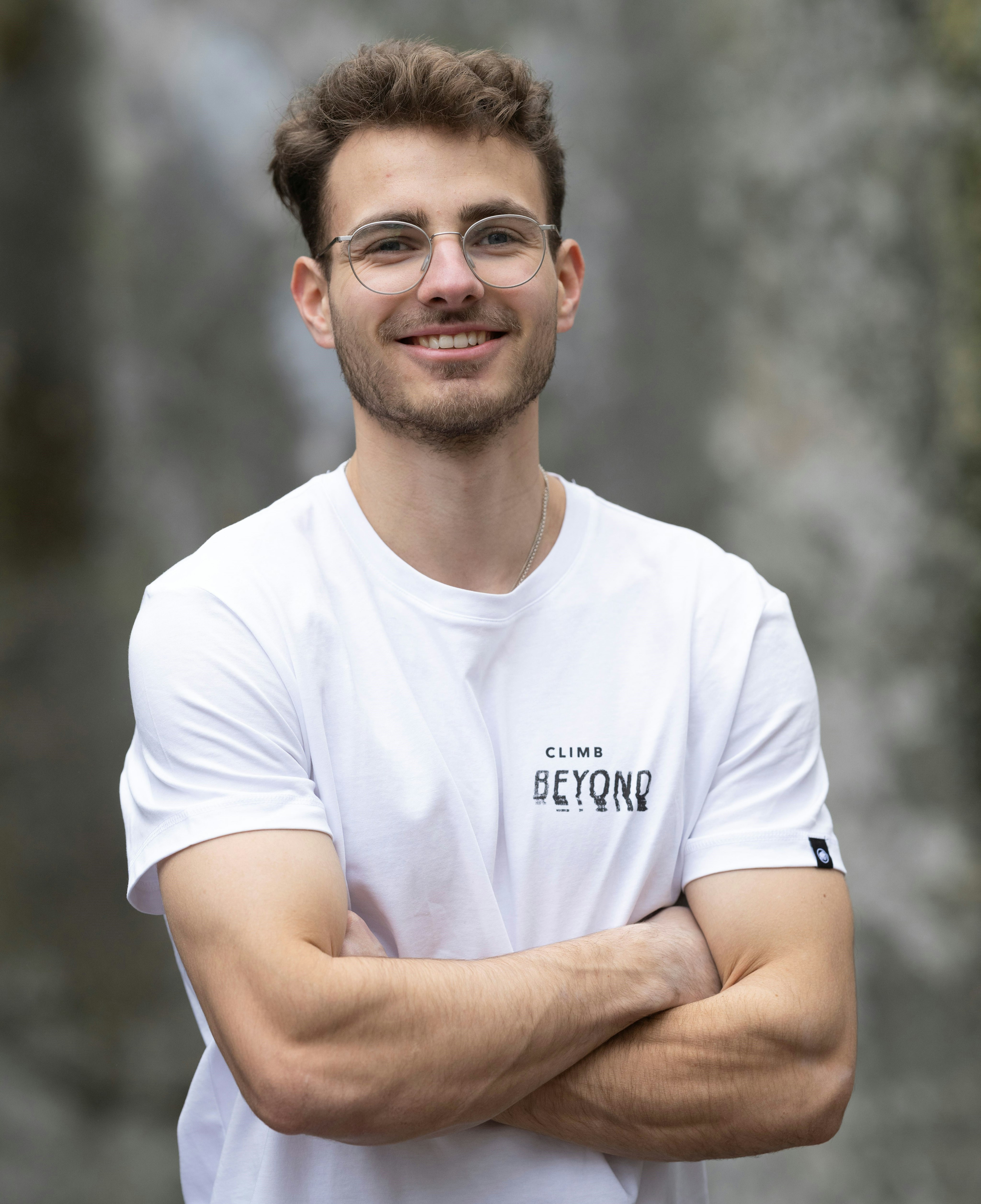 Climber Yannik Flohe wearing a white Mammut T-shirt standing outdoors, smiling with arms crossed.