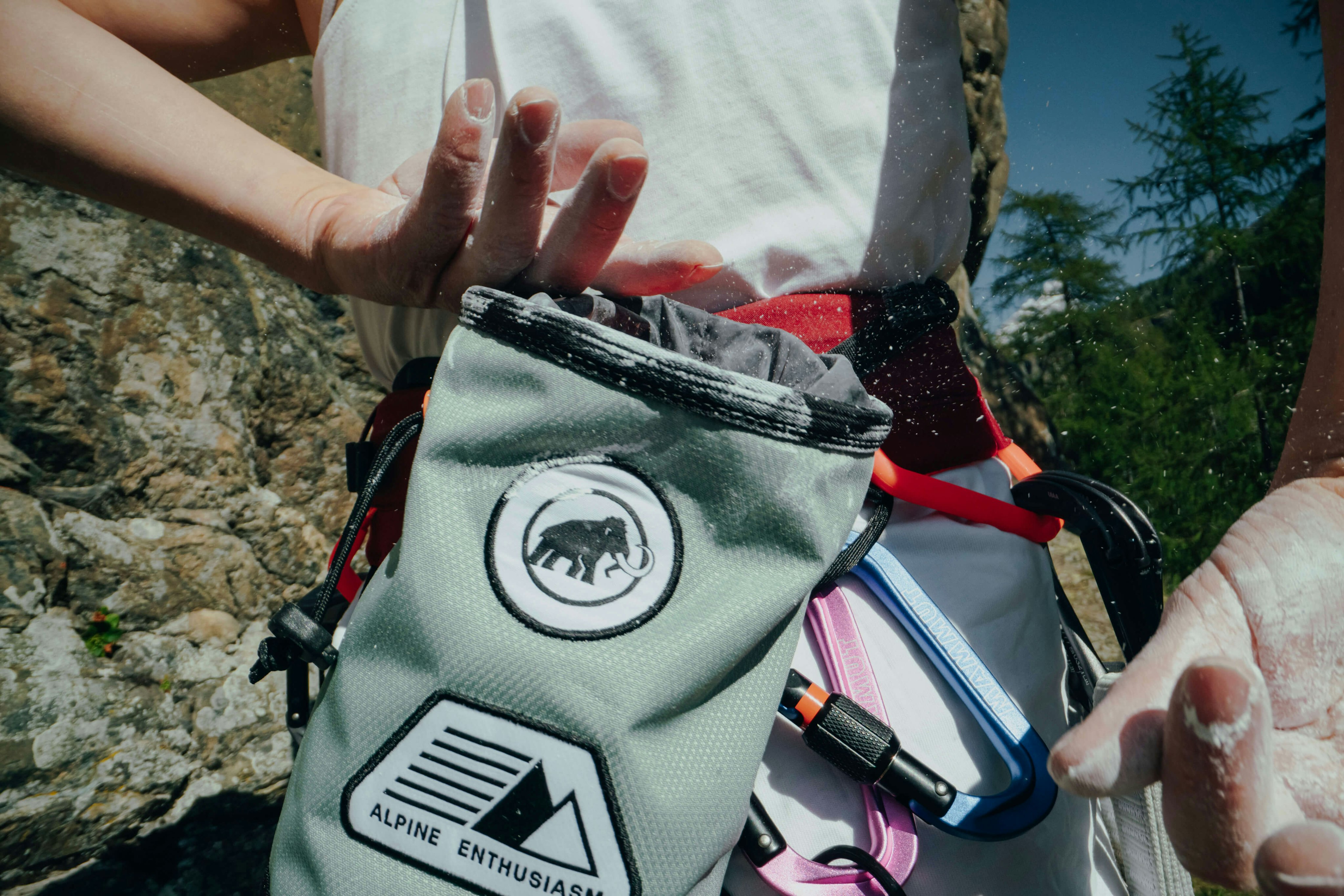 A climber using a Mammut chalk bag applies chalk to their hands outdoors, with Mammut climbing gear attached to their harness.