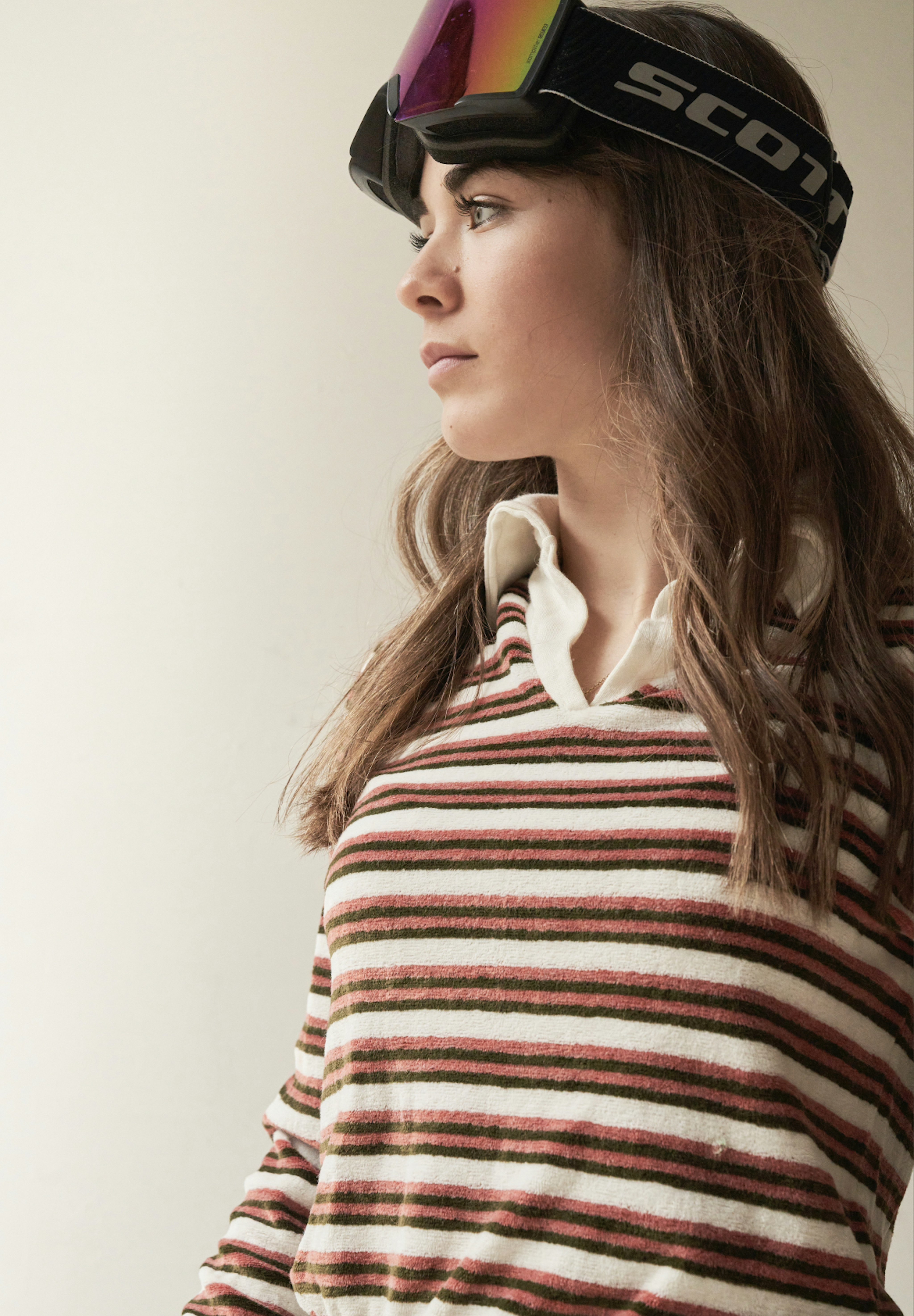 Mammut athlete, Zoe Delzoppo, in striped top with ski goggles resting on her head, gazing to the side against a neutral background.