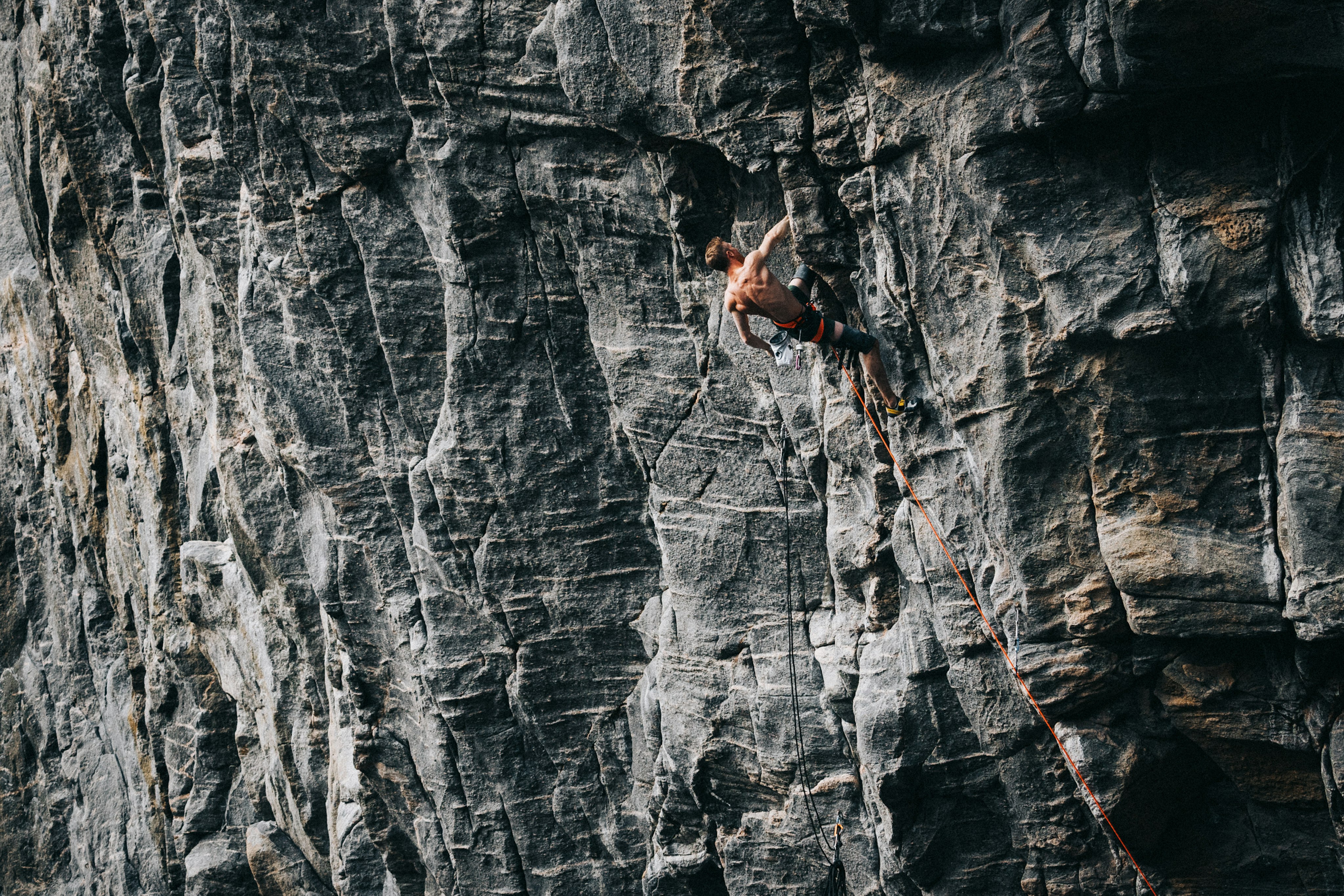 Jakob Schubert climber in a red Mammut shirt scaling a steep, rocky cliff with Mammut ropes and safety gear.