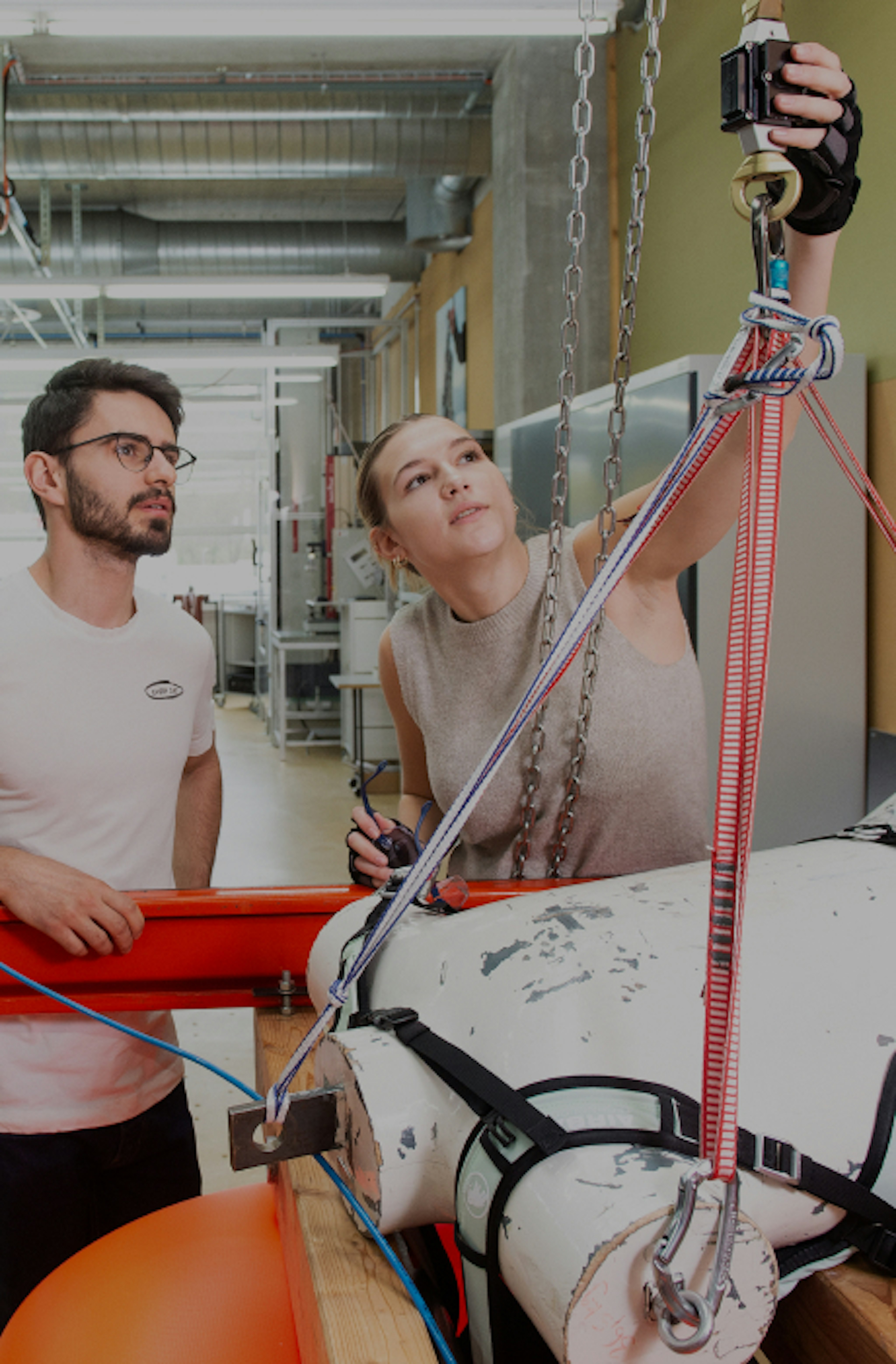 Two individuals utilizing Mammut harnesses and equipment in an industrial environment, concentrating on a suspended object.