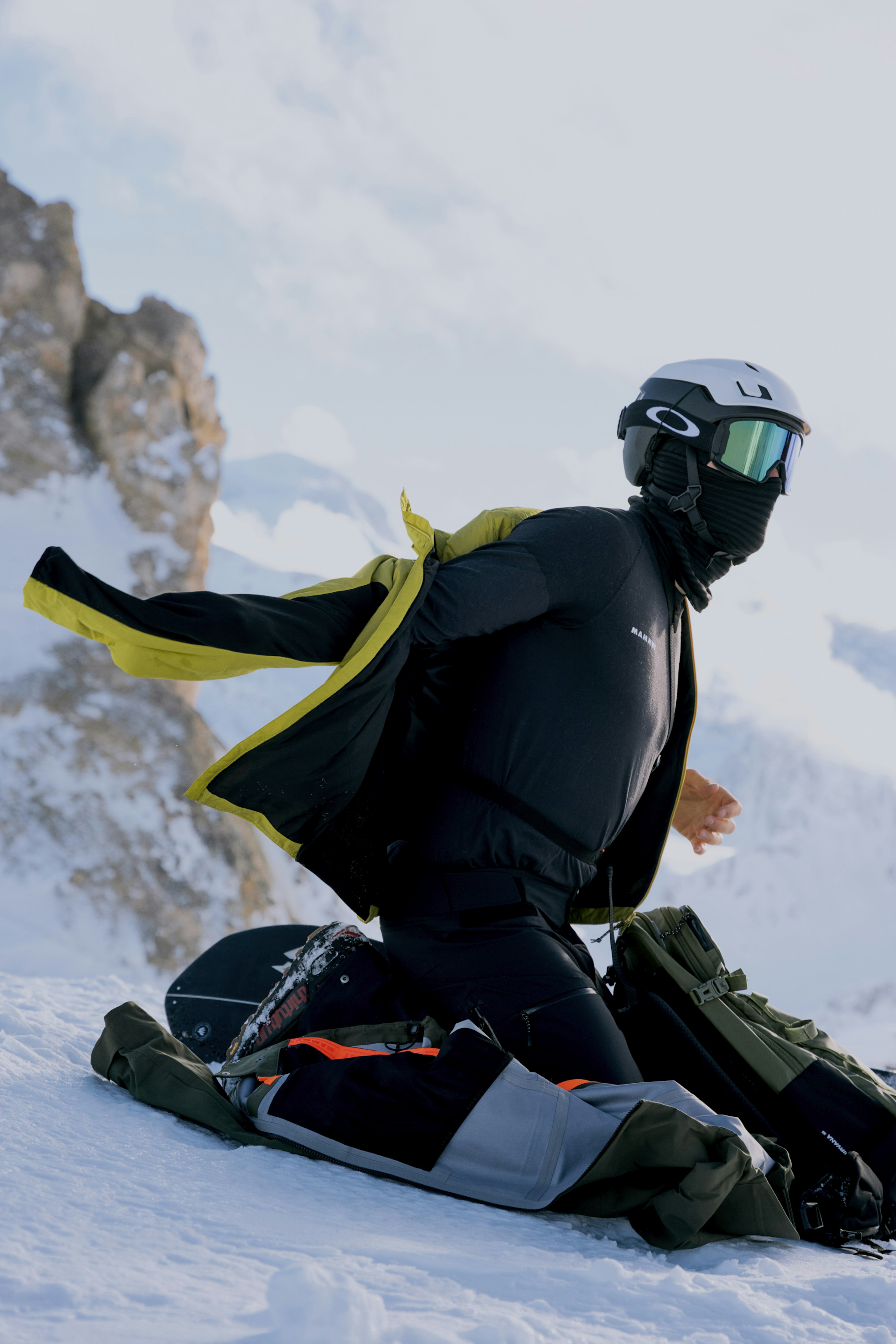 Individual showcasing the label inside a tan Mammut jacket, standing outdoors with scenic hills in the background.