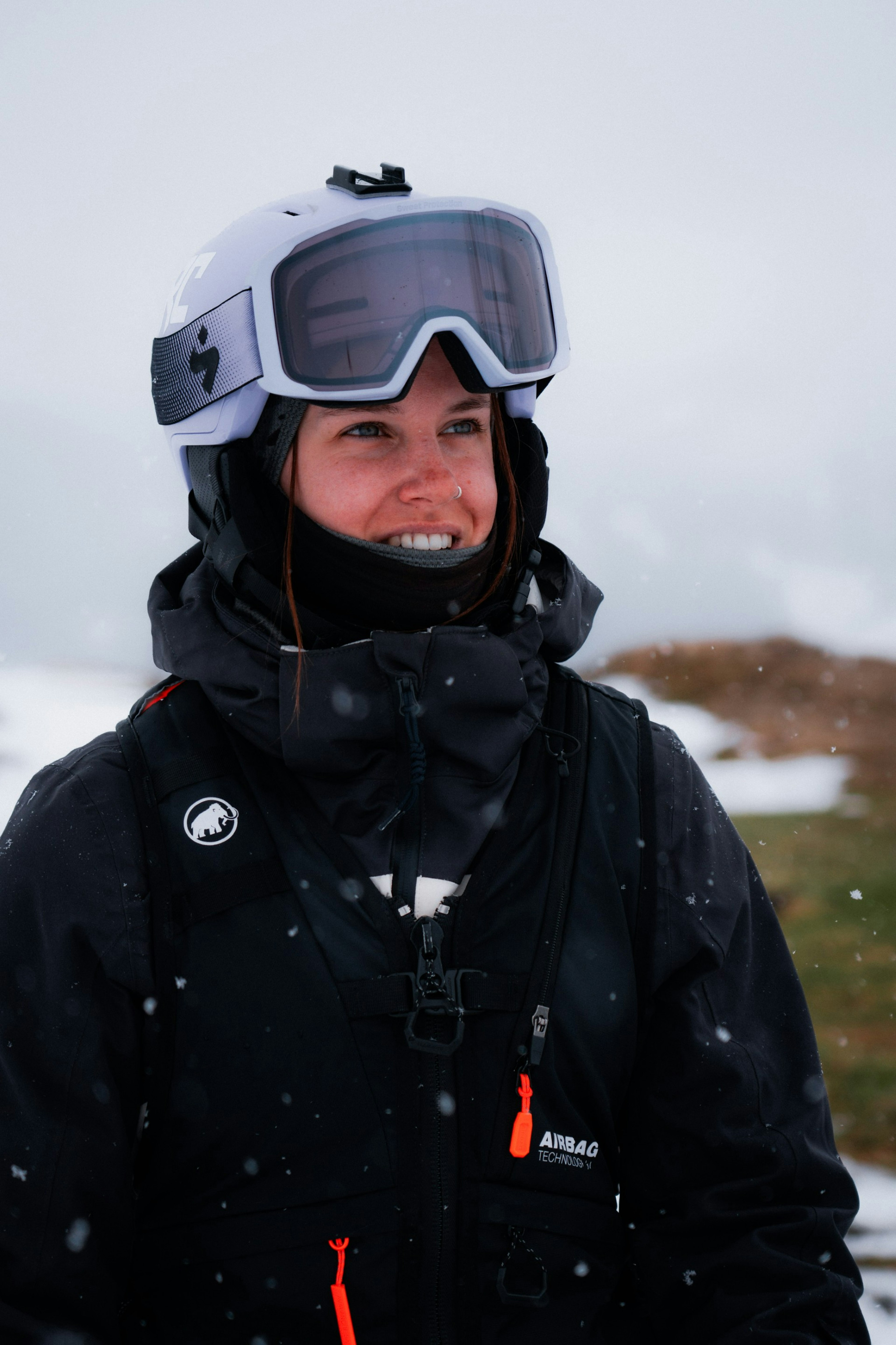 A skier clad in Mammut ski gear, helmet, and goggles smiles outdoors amidst snowy alpine conditions.