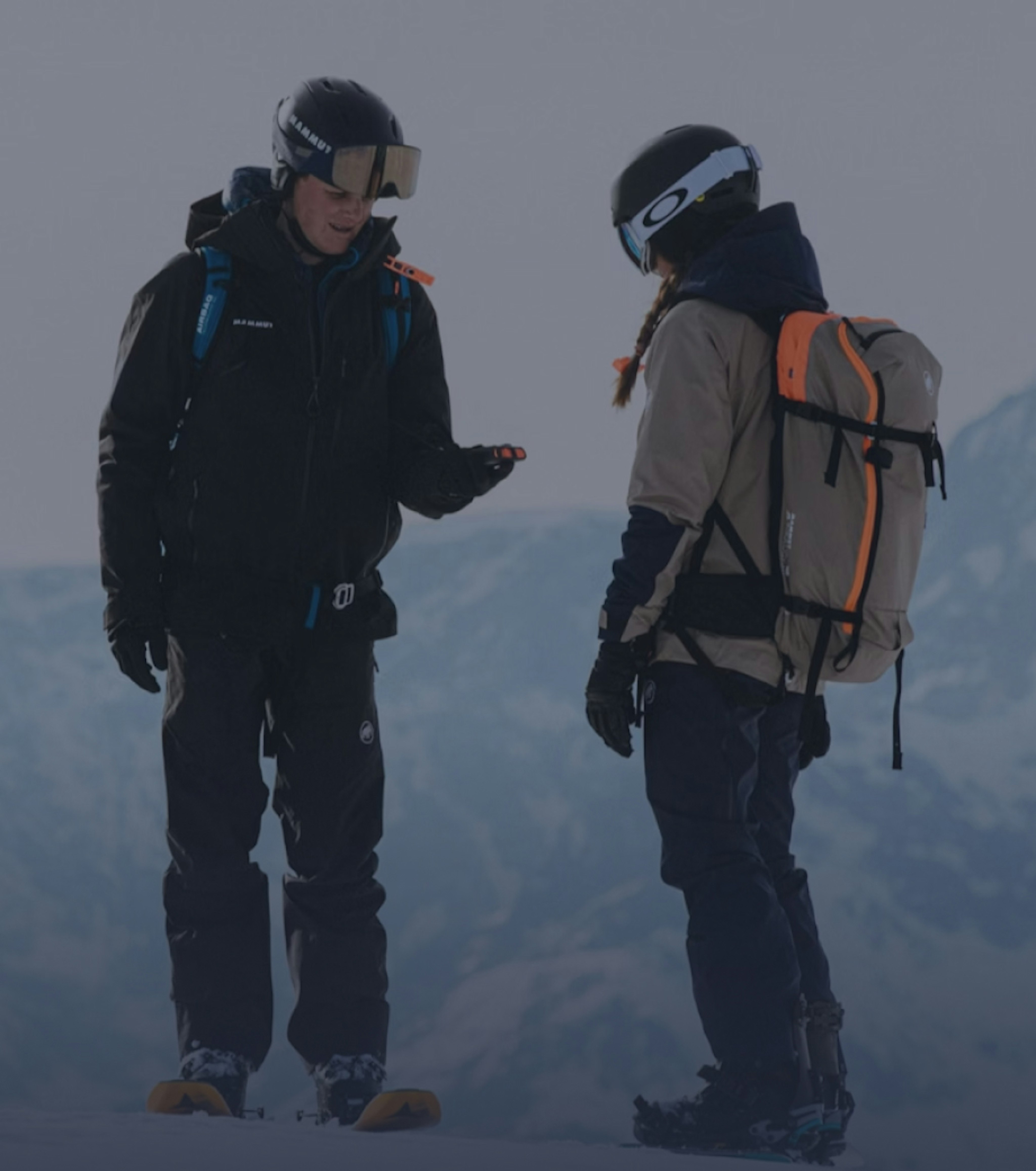 Two people in Mammut skiing gear stand on a snowy Alpine mountain slope, engaged in conversation.