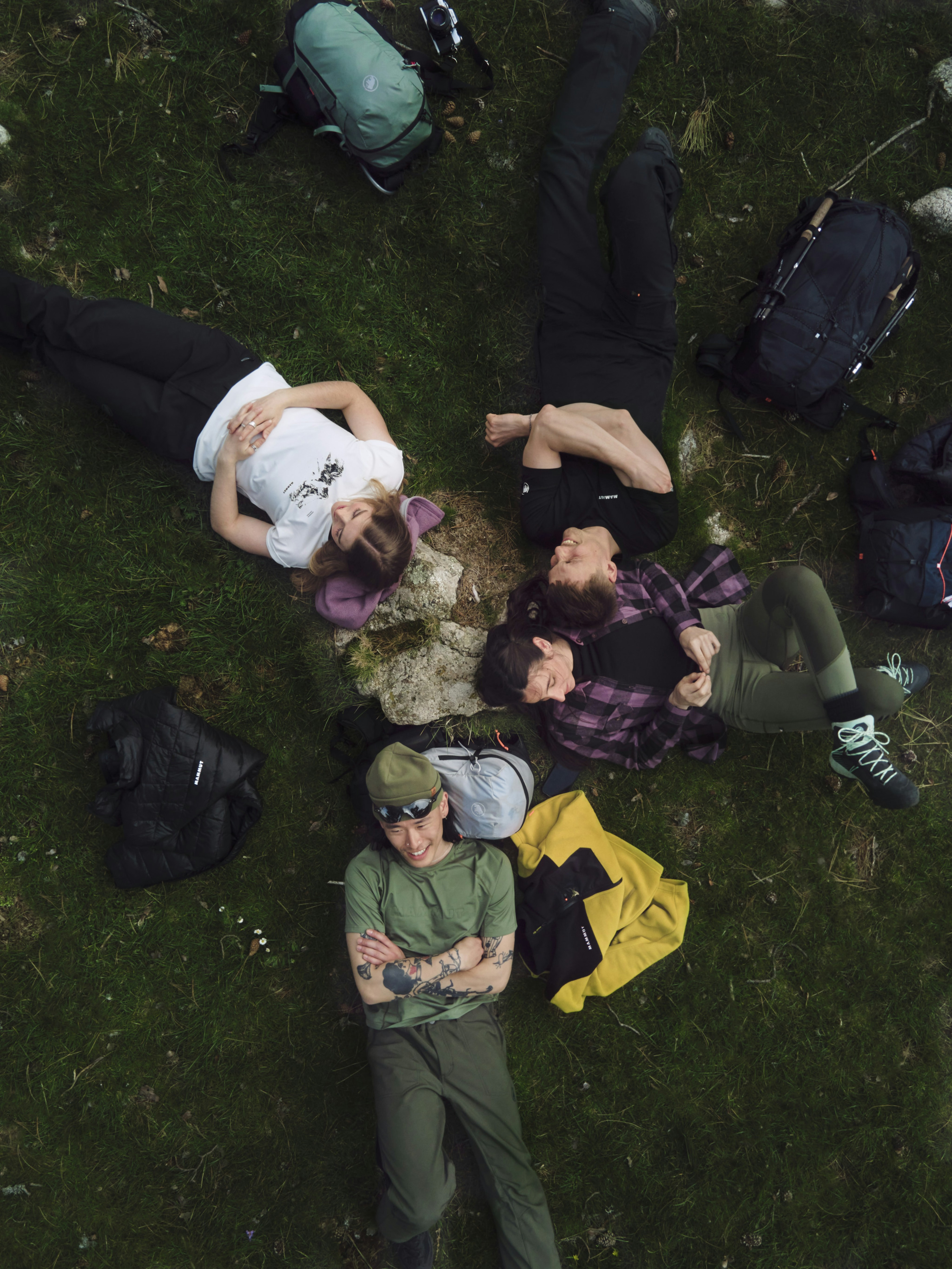 Four people, geared up with Mammut backpacks, lie on the grass enjoying the outdoors during a mountaineering adventure.