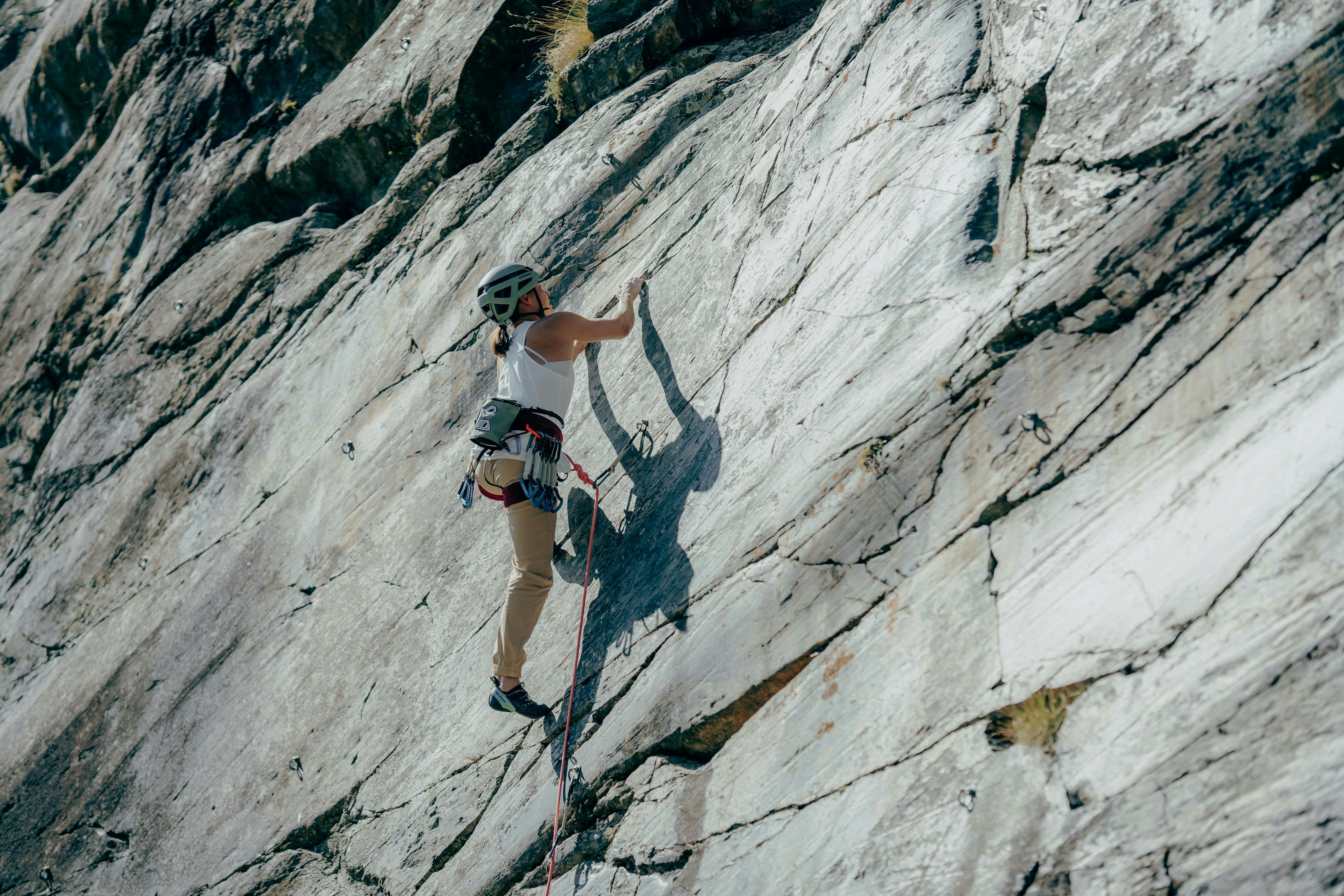 A climber in full Mammut gear scales a steep rock face, utilizing high-quality ropes and safety equipment, with rugged rocky terrain in the background.