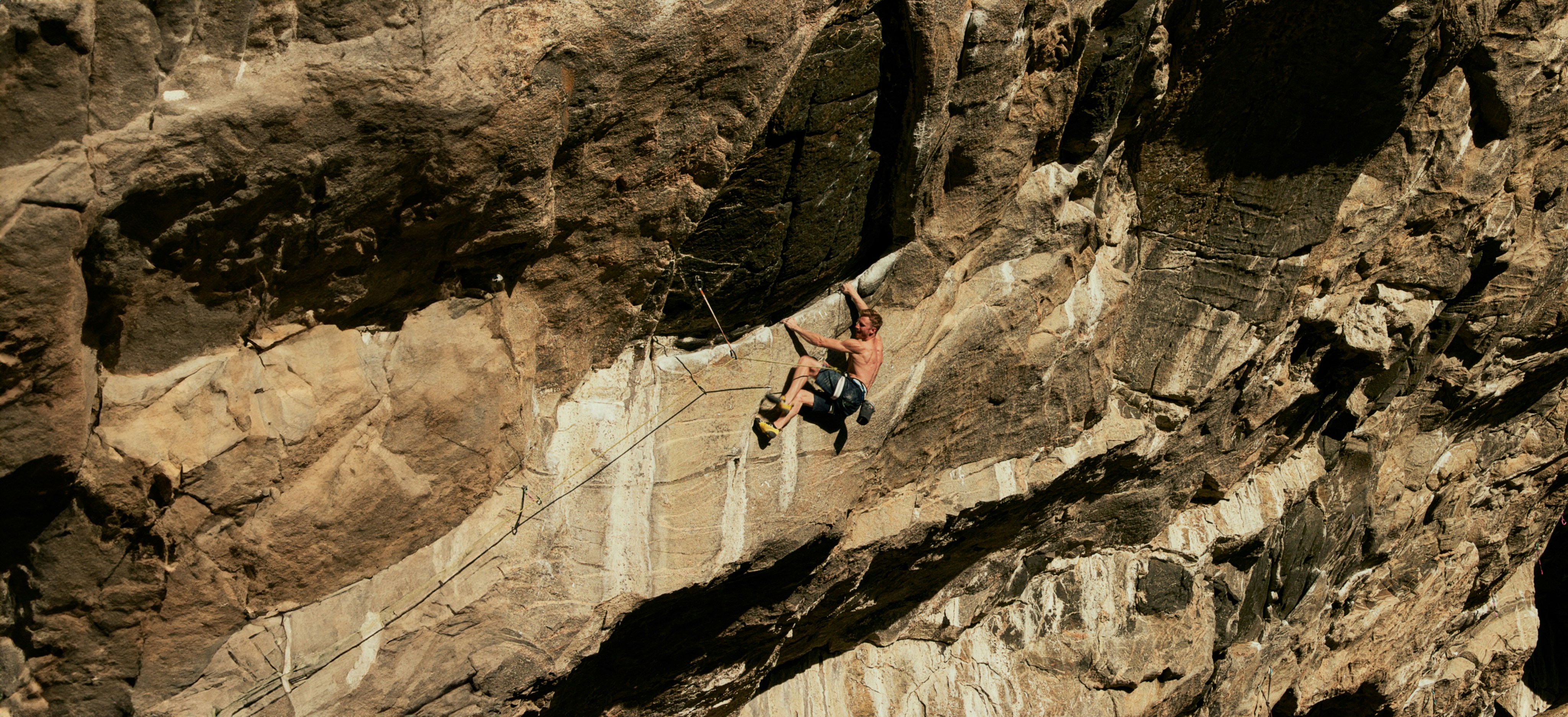 Climber Jakob Schubert in a red Mammut shirt and helmet scaling a steep, rocky cliff.