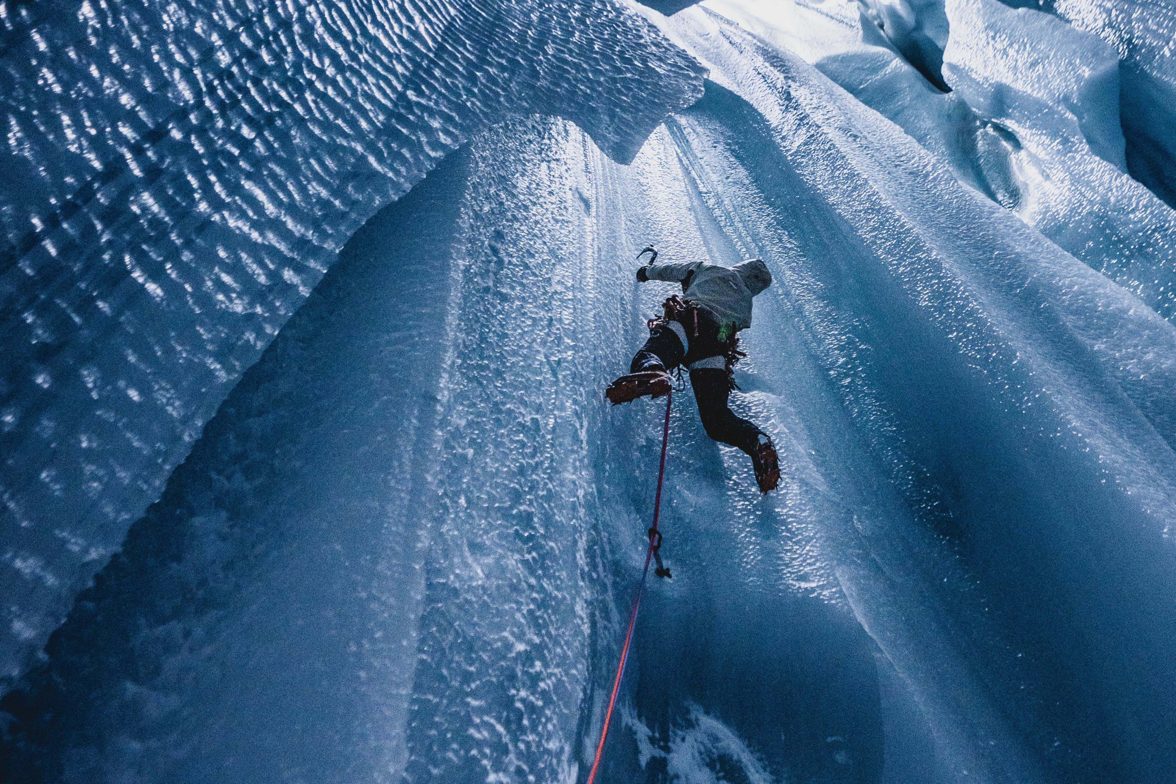 A climber geared up in Mammut equipment skillfully ascends a glistening ice wall using top-notch ice axes and ropes. The intricately textured ice sparkles under the light, showcasing the premium quality of Mammut's climbing gear.